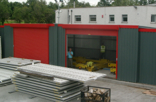 This is a building designed for manfacturing precast wall panels. The wall panels are cast inside the building, concrete is poured throught the two roller shutter doors. When the walls are cured the building can split in the middle and sliding back over the existing building enabling the precast walls to be lifted vertical out of the mould table via a mobile crane